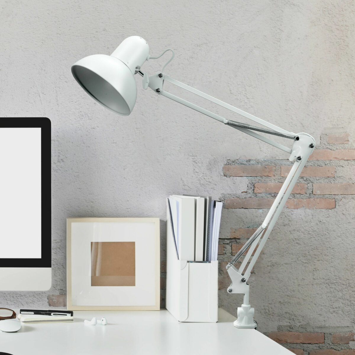 Белая металлическая настольная лампа с регулируемым кронштейном, закрепленная струбциной на краю рабочего стола