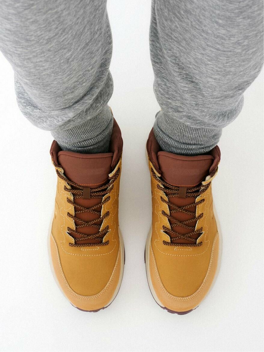 Стильные желто-коричневые ботинки с коричневыми шнурками на фоне серых спортивных брюк