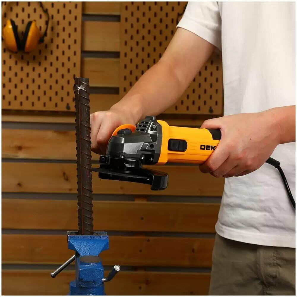 Угловая шлифовальная машина DEKO жёлто-чёрного цвета использует человек для резки металлического прута, зажатого в тисках