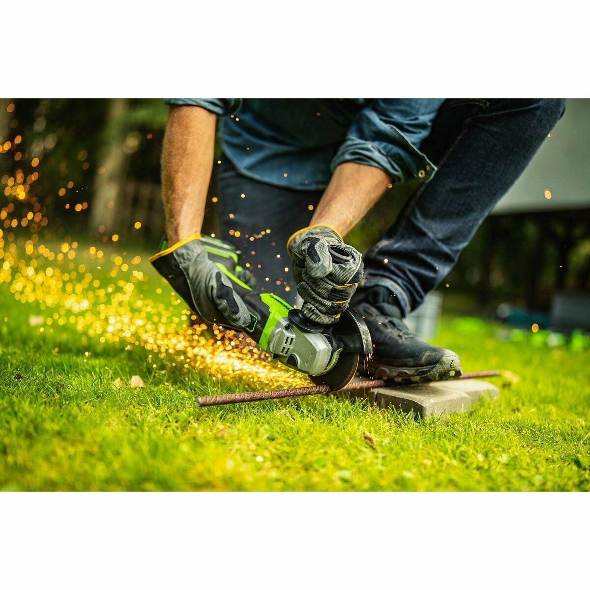 Человек в защитных перчатках режет металлический прут на брусчатке с помощью угловой шлифовальной машины, разлетаются искры