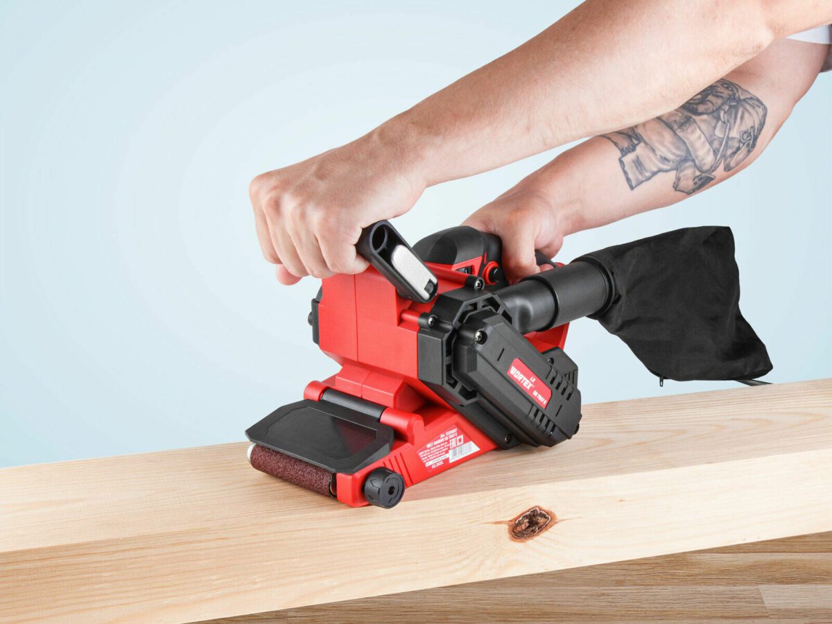 Ручной ленточный шлифовальный станок VORTEX LB 9303 с мощностью 930 Вт и красным корпусом, используется для шлифовки деревянных поверхностей