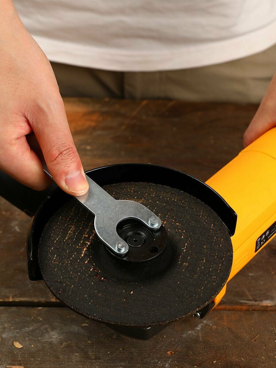 Процесс замены диска на жёлтой угловой шлифовальной машине с использованием крепежного ключа