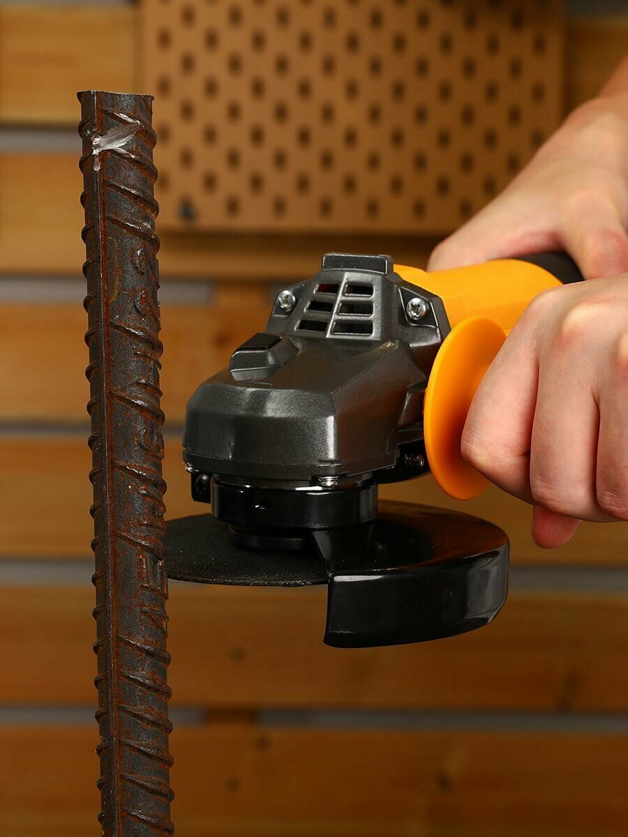 Человек использует угловую шлифовальную машину с черным защитным кожухом и желтой ручкой для обработки арматурного стержня