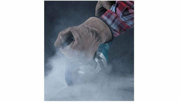 Человек в защитных перчатках использует зеленовато-бирюзовую угловую шлифовальную машину для обработки материала