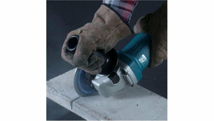 Человек использует синюю углошлифовальную машину с маркировкой '75' и дополнительной ручкой для резки каменного материала, соблюдая меры безопасности