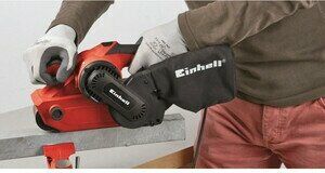 Человек использует красную шлифовальную машину Einhell с логотипом и мешком для сбора пыли, предназначенную для шлифования поверхности