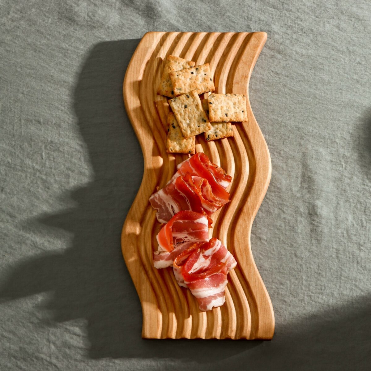 Деревянная доска для подачи из берёзы с волнообразным дизайном и рельефной текстурой на сером фоне