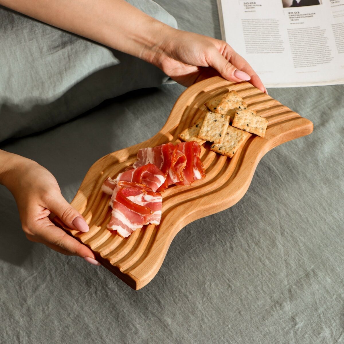 Деревянная доска для подачи из берёзы с натуральной текстурой, украшенная закусками и крекерами на фоне уютной обстановки