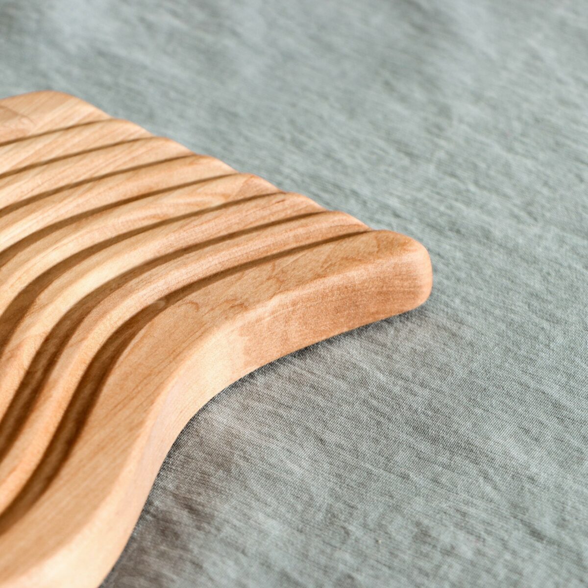 Фрагмент деревянной доски для подачи с волнообразной выемчатой поверхностью и светло-бежевым оттенком