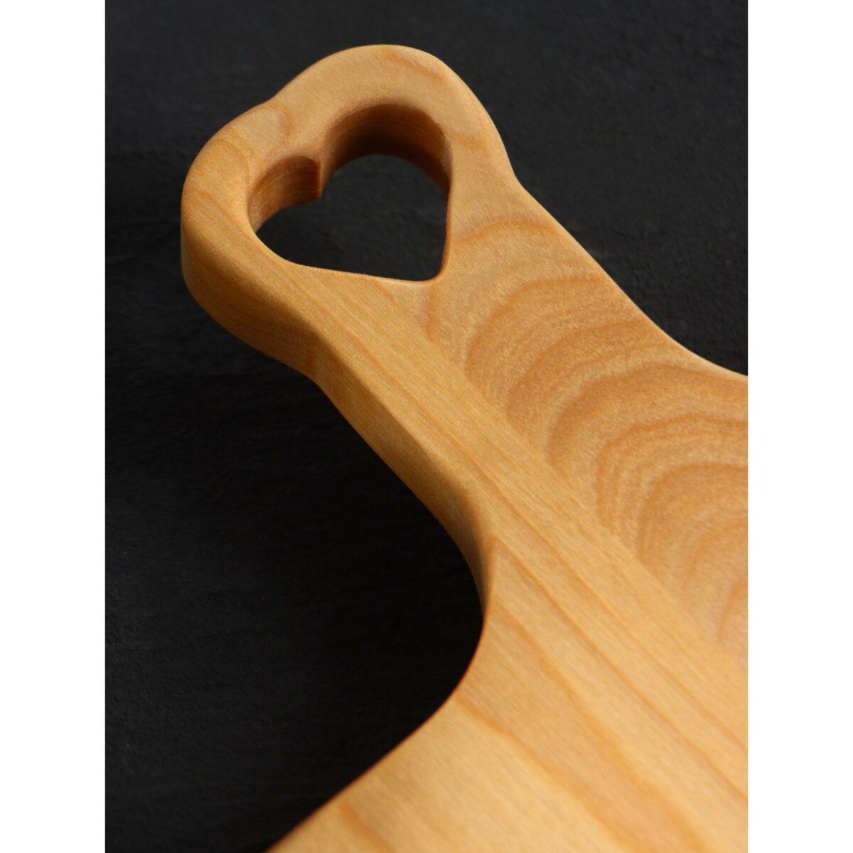 Деревянная разделочная доска с фигурной ручкой в виде сердца – экологичный стильный подарок для кухни Крупный план разделочной доски с фигурной ручкой в виде сердца, выполненной из светлой березовой древесины с выразительной текстурой