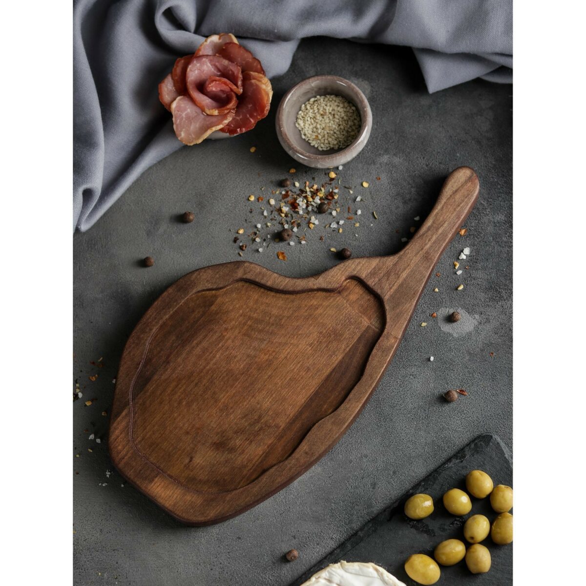 Деревянная доска для подачи мяса и закусок с выемкой — стильный аксессуар для сервировки еды Деревянная доска для подачи мяса и закусок с выемкой, выполненная из берёзовой древесины, с расположенными вокруг продуктами — ветчиной, оливками и сыром