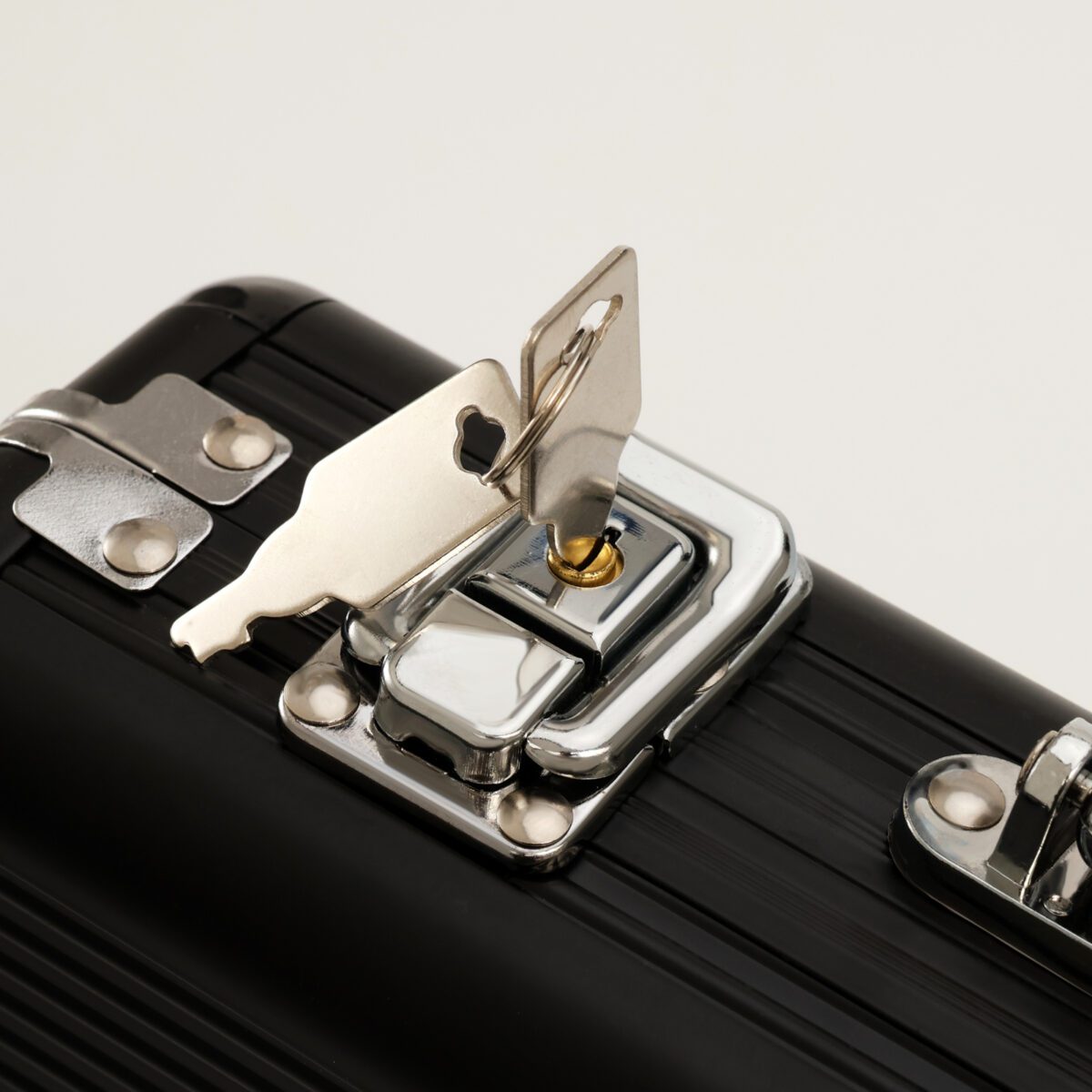 Компактный черный металлический кейс с замком – прочный и универсальный аксессуар для хранения Черный металлический кейс с замком, фрагмент с серебристым ключом и рельефной поверхностью корпуса