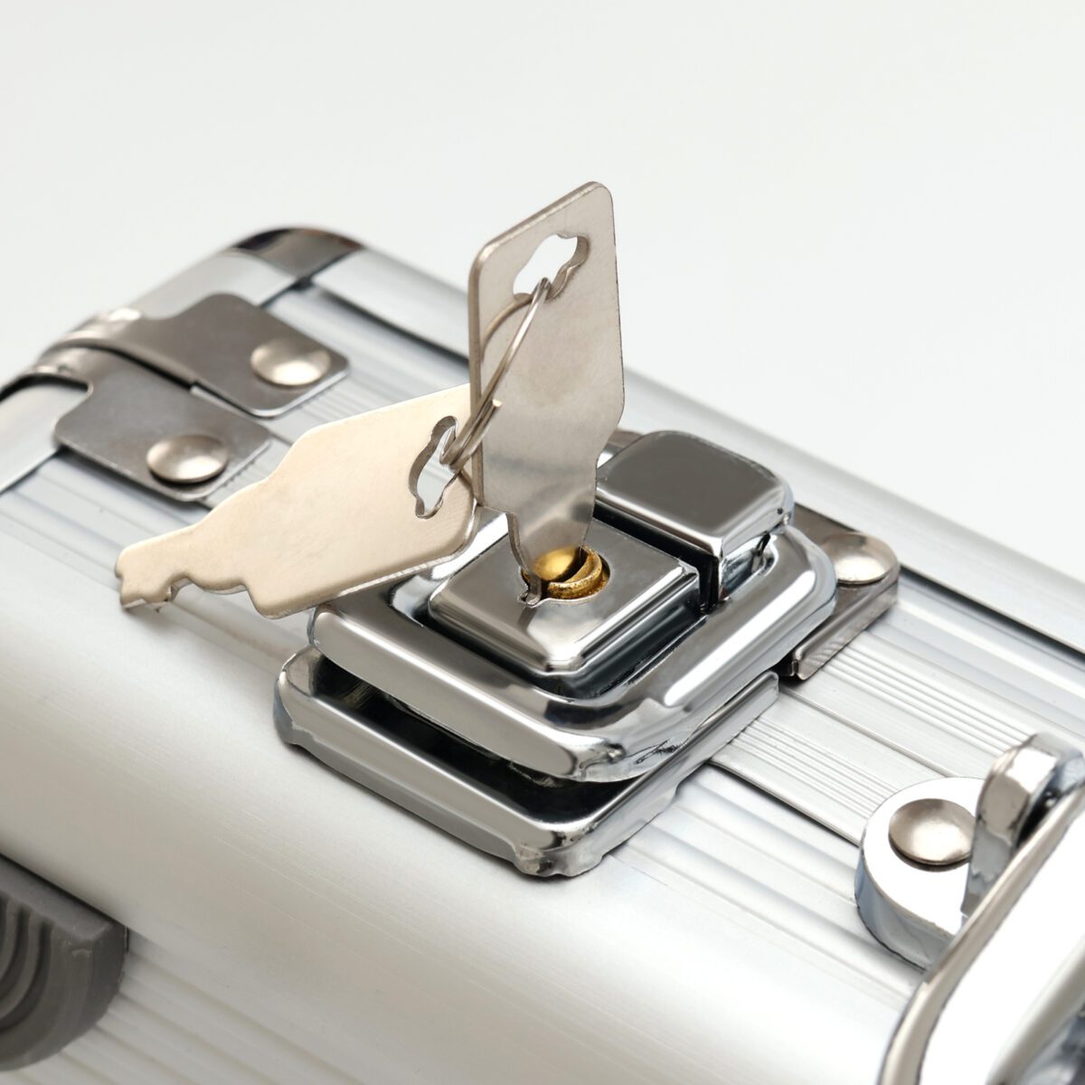 Прочный и стильный металлический кейс с надежным замковым механизмом Замковый механизм металлического кейса с ключами на фоне текстурированной серебристой поверхности