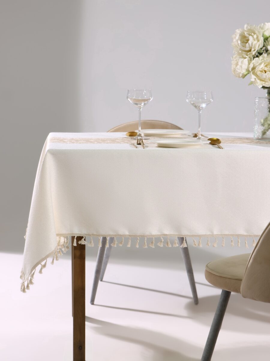 Праздничная прямоугольная скатерть светлого кремового оттенка с бахромой — стильный декор для новогоднего стола Скатерть прямоугольная с бахромой для праздничного украшения стола, сервированного бокалами, тарелками и золотистыми приборами