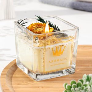 Ароматическая свеча в стеклянной квадратной банке с сушеным цветком и зеленью на фоне уютного интерьера