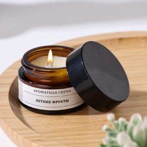 Фигурная свеча натурального аромата из соевого воска в темной стеклянной банке с крышкой, на светлой деревянной подставке