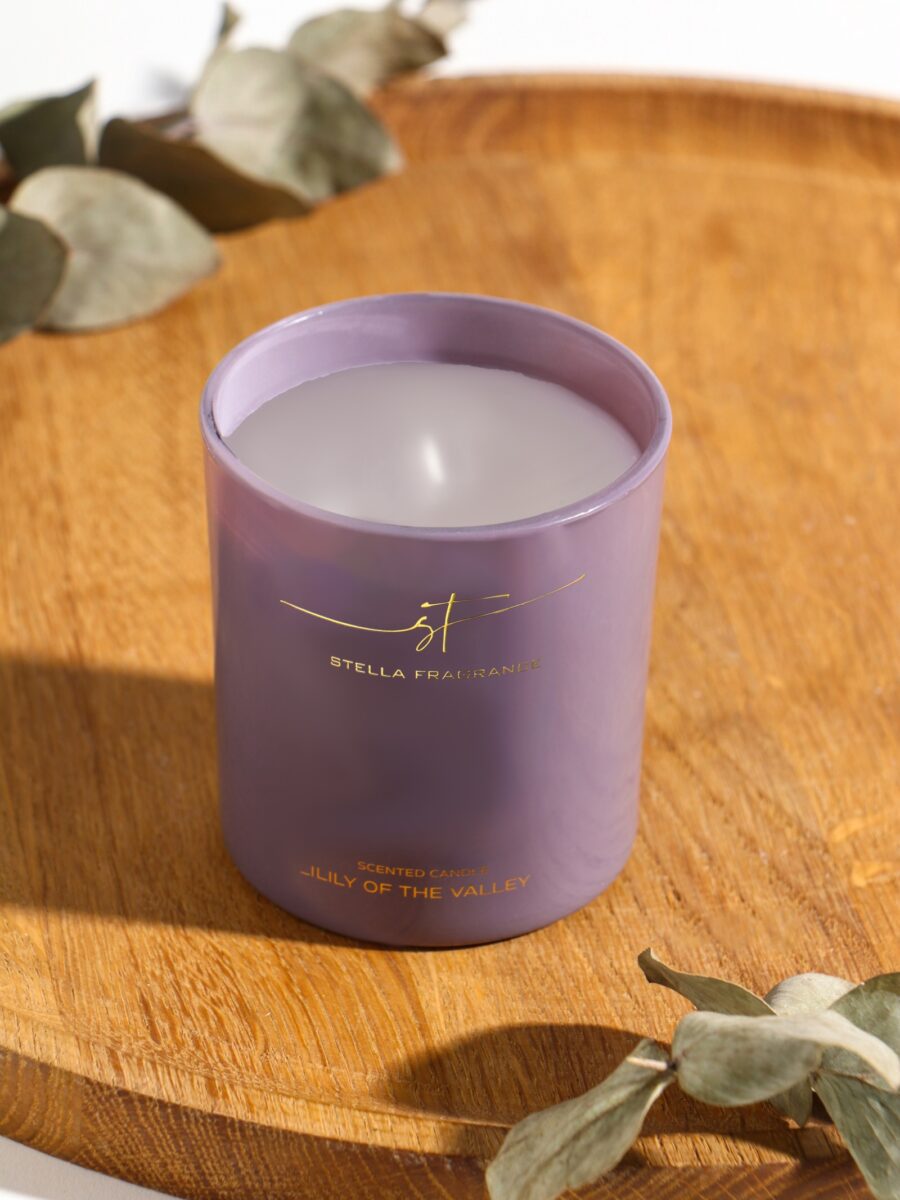 Натуральная ароматическая свеча 160 г с ароматом Ландыш в матовом стеклянном стакане Ароматическая свеча 160 г с ароматом Lily of the Valley в нежно-фиолетовом матовом стакане на деревянной поверхности с декором из сухих эвкалиптовых веток