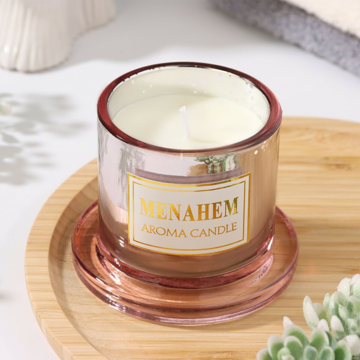 Ароматическая свеча в розовом стакане с деревянным фитилем — стильное украшение для интерьера Натуральная ароматическая свеча в металлическом розовом стакане с белым воском и деревянным фитилем, расположенная на фоне текстиля и растений