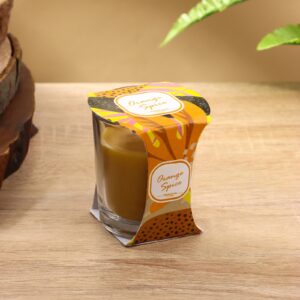 Ароматическая свеча в стеклянном стакане с насыщенным оранжевым воском и упаковкой из картона с элементами оранжевого, желтого и зеленого цветов. Подходит для украшения дома и наполнения пространства ярким ароматом апельсина и специй.