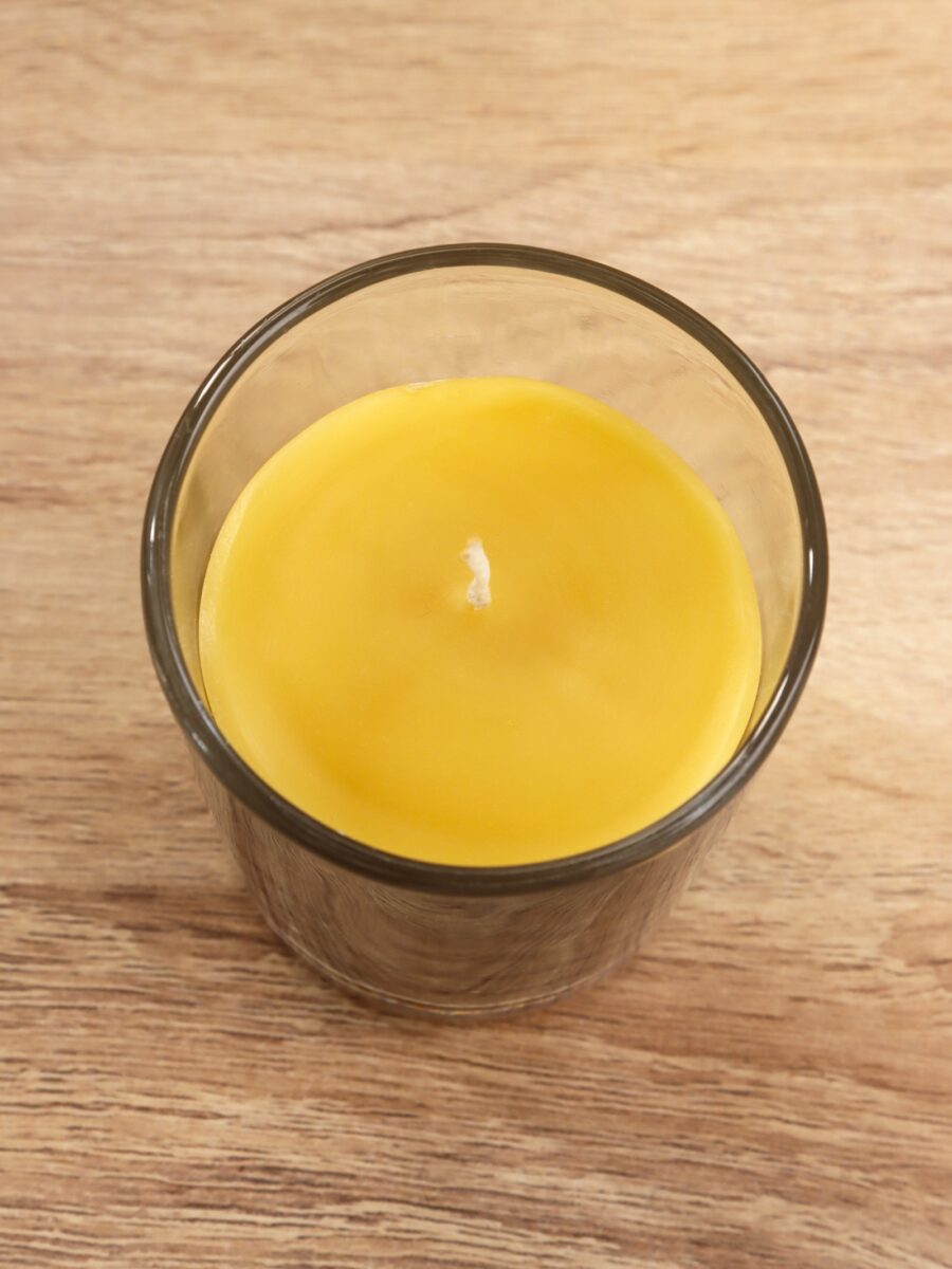 Ароматическая свеча 85 г в стеклянном стакане с ароматом апельсина и специй – уютный декор для дома Натуральная ароматическая свеча 85 г ярко-жёлтого цвета в прозрачном стеклянном стакане на деревянной поверхности