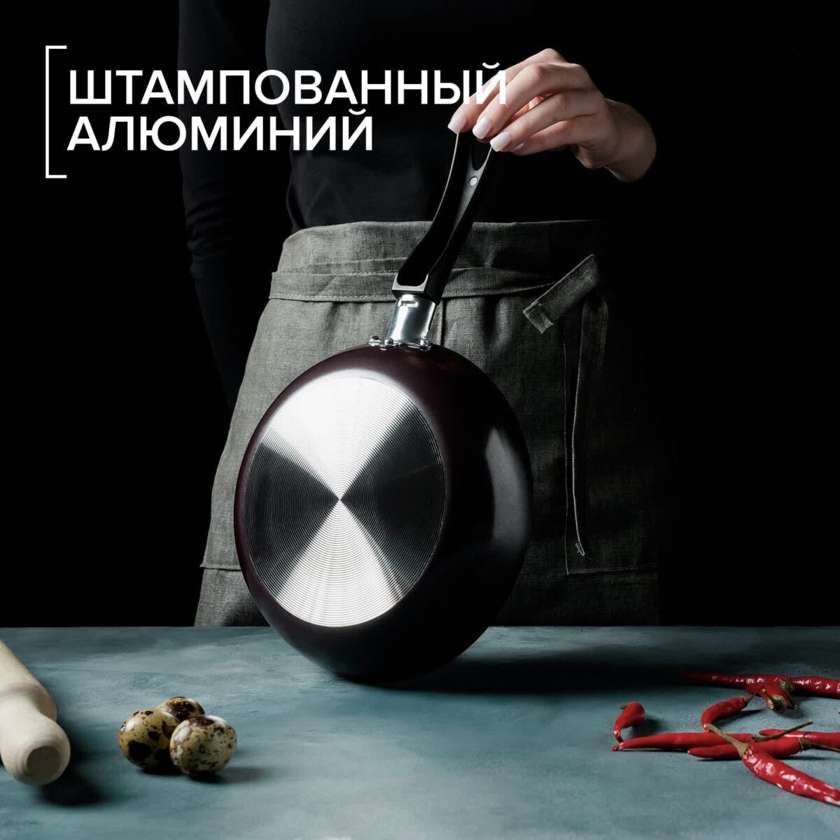 Сковорода из штампованного алюминия с бордовым корпусом и эргономичной ручкой, 22 см Сковорода диаметром 22 см из штампованного алюминия, бордового цвета с пластиковой ручкой, на фоне кухни с ингредиентами